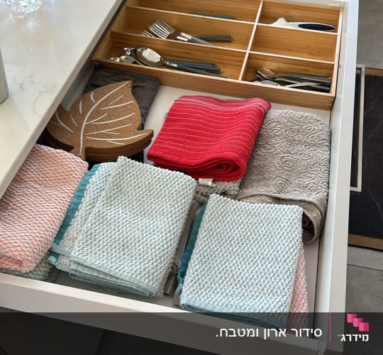 מגבות ומפיות מסודרות במגירה עם סכו"ם ומחלקת עץ